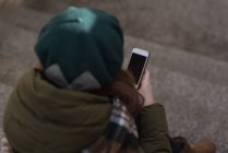 Frau in Winterkleidung benutzt Handy im Treppenhaus — Stockfoto