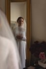 Kaukasische Braut in Brautkleid und Schleier blickt in Vintage-Boutique in den Spiegel — Stockfoto