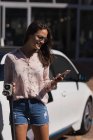 Frau benutzt Handy beim Halten von Ladestecker an Ladestation — Stockfoto
