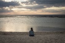 Вид ззаду жінки, що сидить на пляжі в сутінках — стокове фото