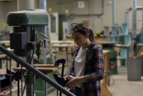 Carpintero femenino con pinza de tornillo en un trozo de madera en el taller - foto de stock
