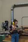 Женщина-плотник осматривает кусок дерева во время использования цифровой планшет в мастерской — стоковое фото