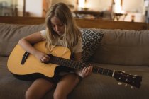 Дівчина грає на акустичній гітарі у вітальні вдома — стокове фото
