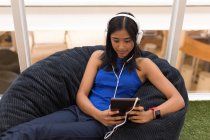 Жінка використовує цифровий планшет під час прослуховування музики на навушниках в офісі — стокове фото