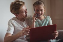 Madre e figlia che parlano sul cellulare mentre utilizzano il computer portatile in soggiorno a casa — Foto stock