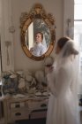 Кавказская невеста в свадебном платье и вуали, смотрящая в зеркало в винтажном бутике — стоковое фото