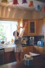 Вид сзади женщины, стоящей с поднятыми руками на кухне дома — стоковое фото