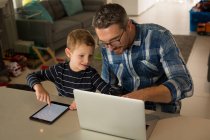Padre e hijo usando portátil y tableta digital en casa - foto de stock