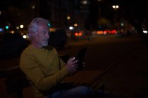 Старший чоловік використовує цифровий планшет у місті вночі — стокове фото