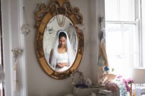 Reflection of young bride in wedding dress in mirror — Stock Photo