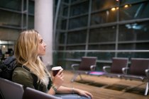 Mulher tomando café enquanto espera na área de espera no terminal do aeroporto — Fotografia de Stock