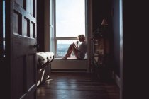 Продумана жінка сидить біля вікна вдома — стокове фото