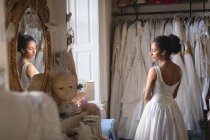 Femme métisse, mariée en robe blanche regardant par la fenêtre à la boutique — Photo de stock