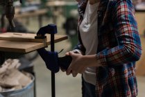 Средняя часть женского плотника с помощью винтового зажима на куске дерева в мастерской — стоковое фото