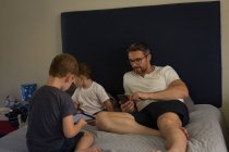 Father and son using mobile phone and digital tablet in bedroom at home — Stock Photo