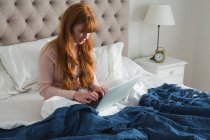 Woman with red hair using laptop in bedroom at home — Stock Photo
