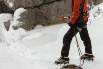 Scalatore femminile che tiene una corda vicino alla montagna rocciosa durante l'inverno — Foto stock