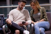 Пара за допомогою мобільного телефону в зоні очікування в аеропорту — стокове фото