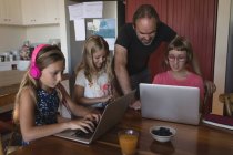 Padre e hijas usando computadoras portátiles en la cocina en casa - foto de stock