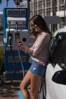 Femme utilisant un téléphone portable tout en rechargeant la voiture électrique à la station de charge — Photo de stock