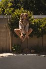 Девушка прыгает на батуте в саду в солнечный день — стоковое фото