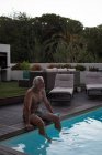 Homem idoso ativo sentado na borda da piscina — Fotografia de Stock