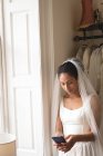 Young bride in wedding dress using mobile phone in the boutique — Stock Photo