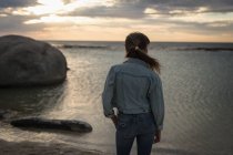Вид ззаду жінки, дивлячись на пляж в сутінках — стокове фото