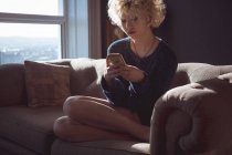 Mulher usando telefone celular na sala de estar em casa — Fotografia de Stock