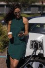 Frau benutzt Handy beim Laden von Elektroauto an Ladestation — Stockfoto