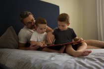Father and sons looking at family album in bedroom at home — Stock Photo