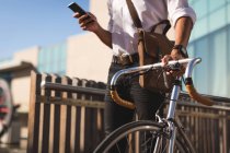 Homme d'affaires utilisant un téléphone portable tout en marchant avec son vélo dans les locaux du bureau — Photo de stock