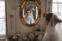 Noiva caucasiana em vestido de noiva e véu olhando para o espelho na boutique vintage — Fotografia de Stock