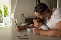 Батько і син снідають під час використання цифрового планшета вдома — стокове фото