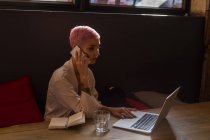 Mujer con estilo utilizando el ordenador portátil, mientras que el hombre habla en el teléfono móvil en el restaurante - foto de stock