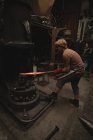 Blacksmith shaping hot metal rod in machine at workshop — Stock Photo