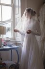 Young bride in wedding dress standing near window at boutique — Stock Photo