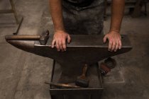 Schmied steht mit Händen auf Amboss in Werkstatt — Stockfoto