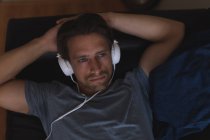 Hombre escuchando música en los auriculares en la sala de estar en casa - foto de stock