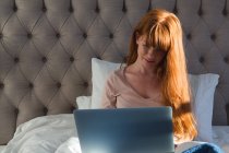 Femme aux cheveux roux utilisant un ordinateur portable dans la chambre à coucher à la maison — Photo de stock
