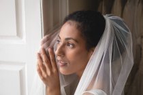 Портрет невесты в свадебном платье и вуали, смотрящей в окно — стоковое фото