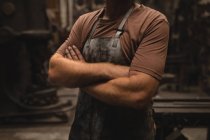 Mid section of blacksmith standing with arms crossed in workshop — Stock Photo
