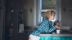 Frau benutzt Handy in Küche zu Hause — Stockfoto
