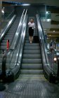 Frau steht mit Gepäck auf Rolltreppe am Flughafen — Stockfoto