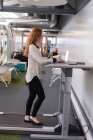 Femme exécutive utilisant un ordinateur portable tout en faisant de l'exercice sur tapis roulant au bureau — Photo de stock