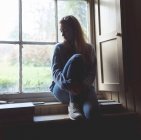 Femme réfléchie se détendre près de la fenêtre à la maison — Photo de stock