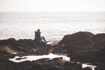 Vista trasera de la mujer sentada en una roca en la playa - foto de stock
