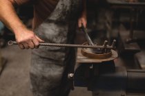 Blacksmith shaping a metal rod in workshop — Stock Photo