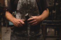 Mid section of blacksmith holding a hammer in workshop — Stock Photo