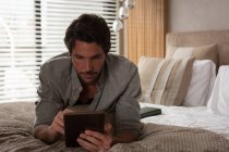 Hombre usando tableta digital en el dormitorio en casa - foto de stock